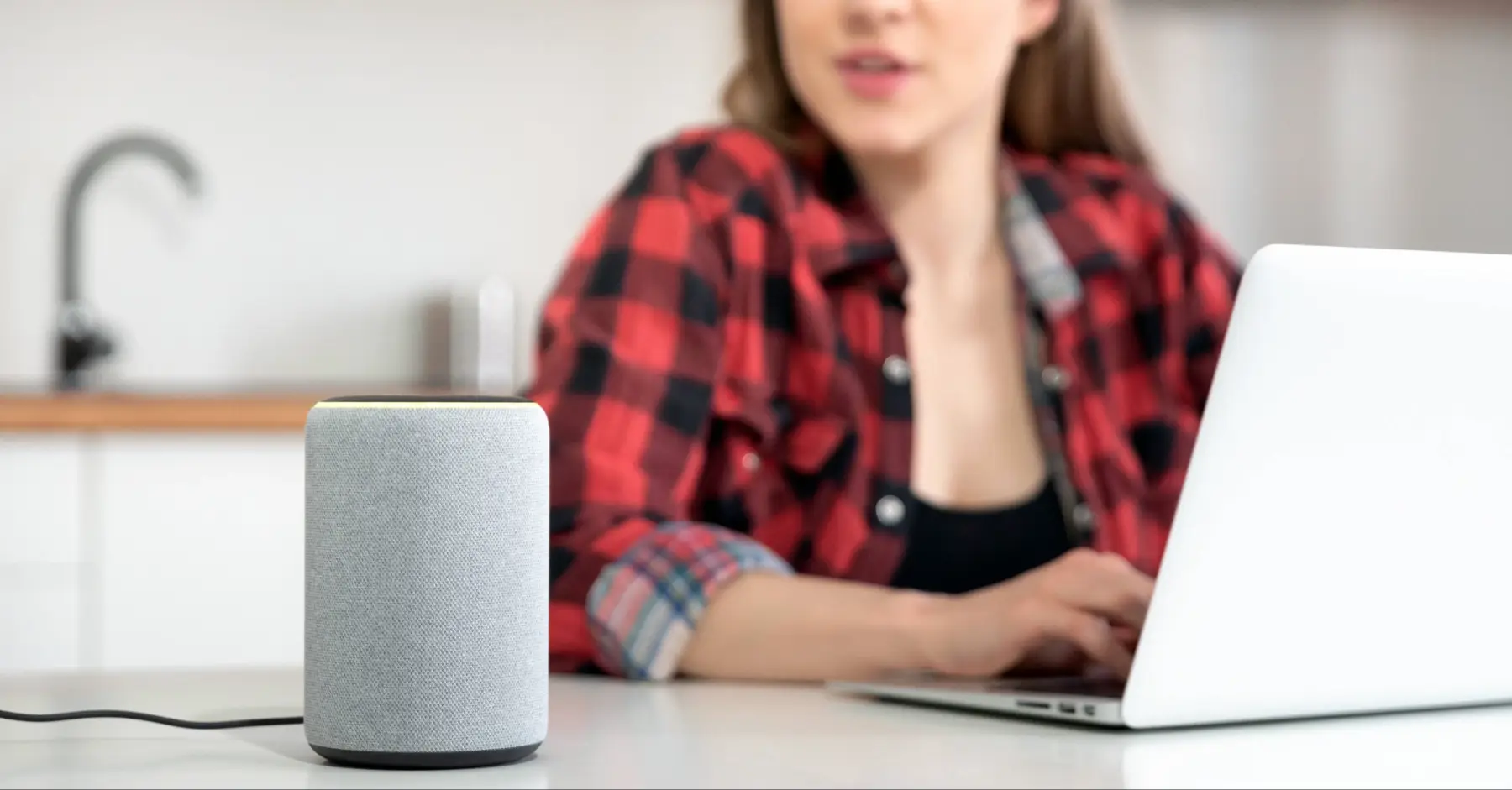 A woman is speaking to a smart home speaker device, asking a question.